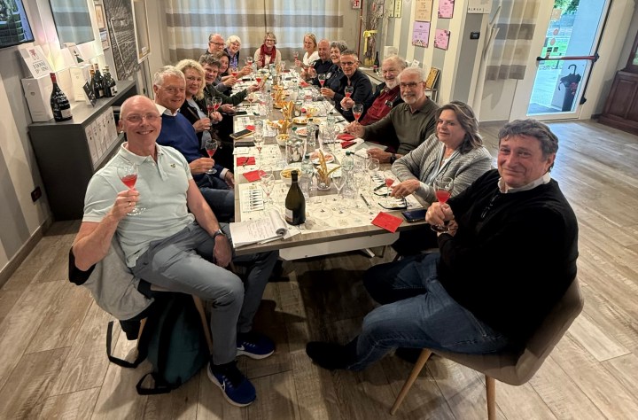 A group of people gathered around a long dining table, smiling and holding drinks during a celebration or social event.