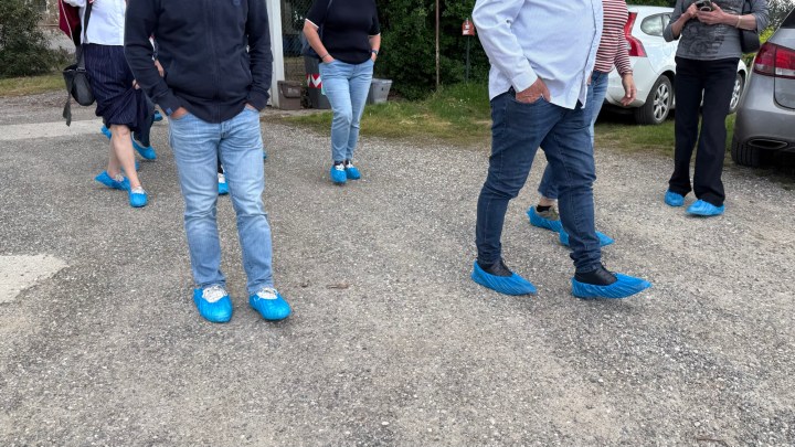 A group of people walking on a gravel path, all wearing blue shoe covers.