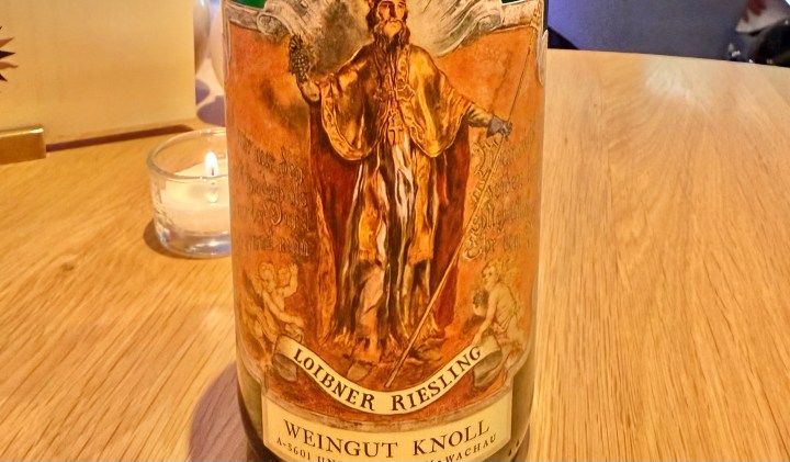 A bottle of Weingut Knoll Loibner Riesling wine, featuring a prominent label with a detailed illustration of a historical figure holding a staff, flanked by cherubs.