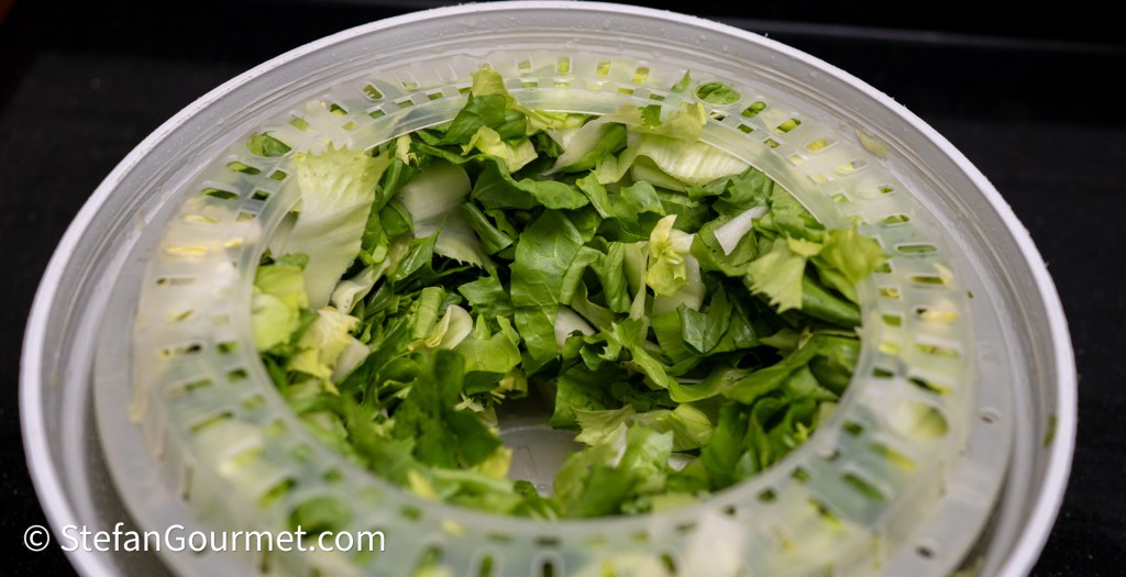 Close-up of a salad spinner filled with freshly washed and chopped green lettuce.