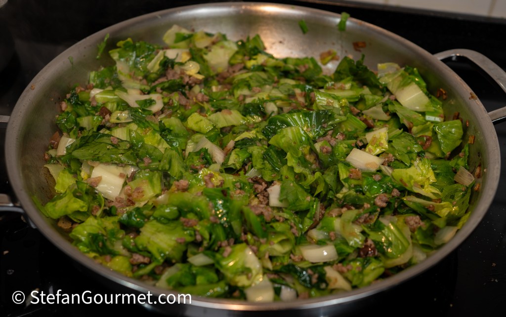 A skillet filled with sautéed green leafy vegetables mixed with browned ground meat, showcasing a vibrant, healthy dish.