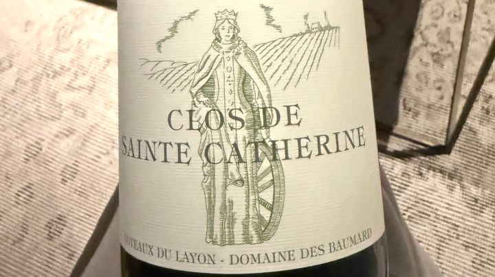 A close-up of a wine bottle label featuring 'Clos de Sainte Catherine' with an illustration of a figure surrounded by vineyards.