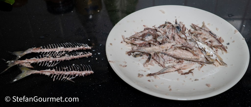 Plate of shredded fish on a black countertop, with fish bones placed beside it.