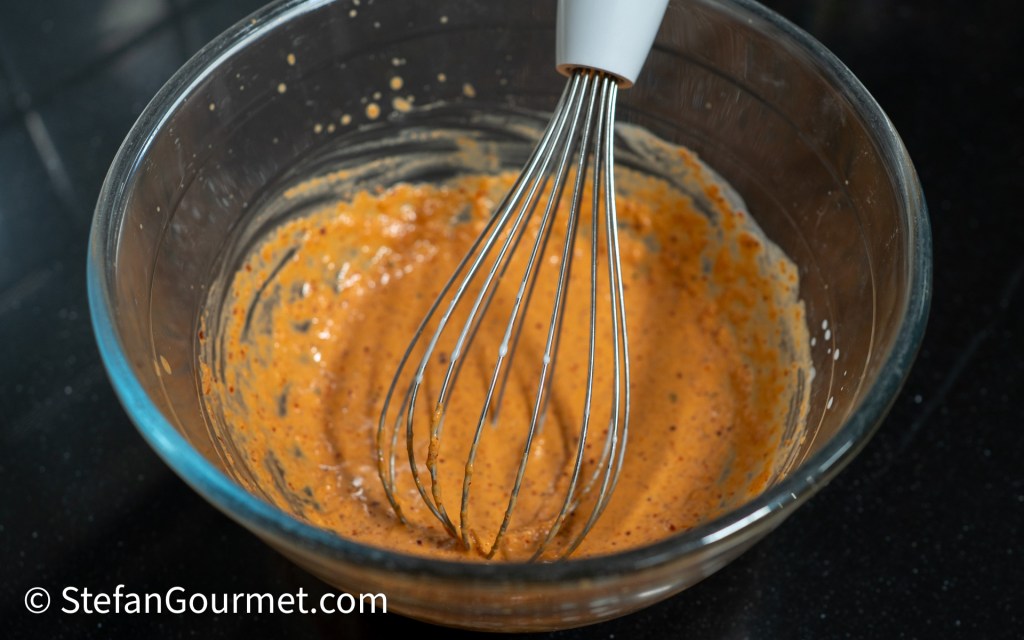 A glass mixing bowl containing a creamy orange mixture with a whisk resting inside.