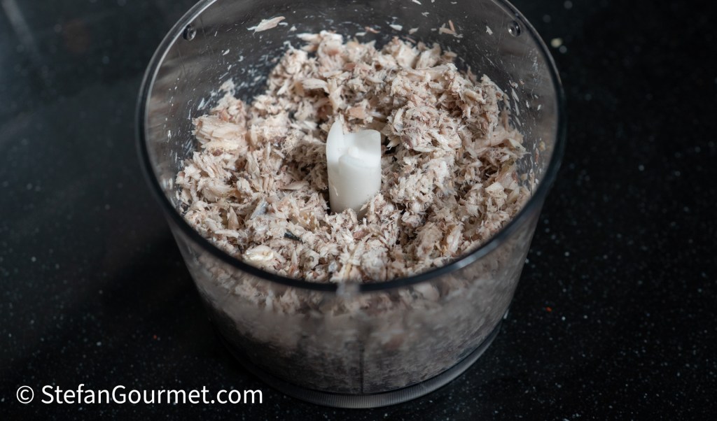 A food processor containing finely shredded or chopped meat, with a white plastic blade in the center.