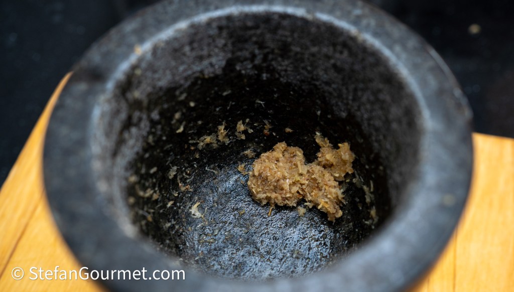 Close-up of a stone mortar with a small amount of brown paste inside.