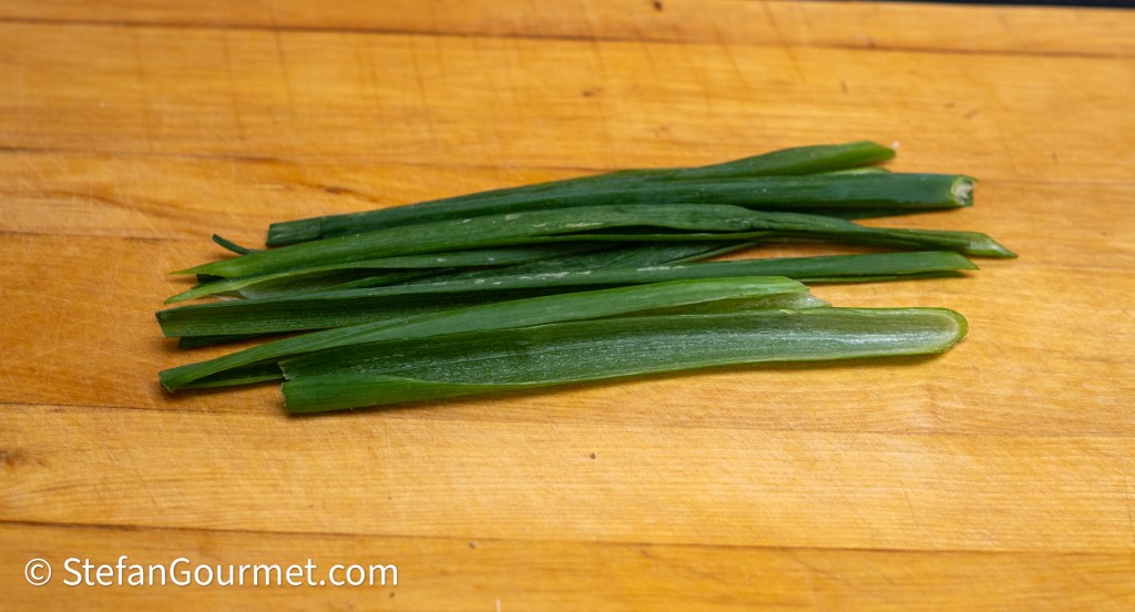 Fresh green onion stalks arranged on a wooden cutting board.