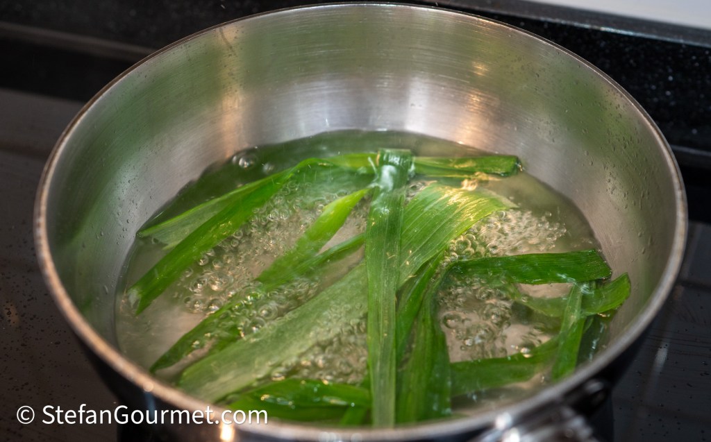 A metal pot with boiling water and green leaves cooking inside.