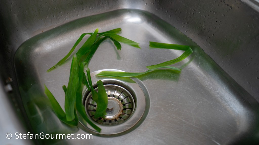Fresh green herbs resting in a stainless steel sink.