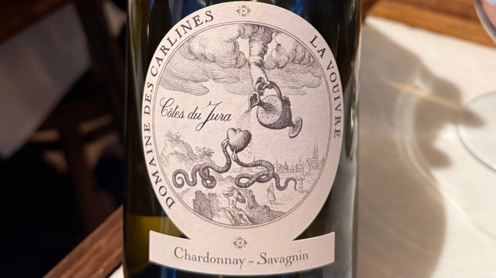 Label of Domaine des Carlines La Vouivre wine bottle featuring a detailed illustration with clouds and a snake intertwined with a heart, labeled as Chardonnay-Savagnin from Côtes du Jura.