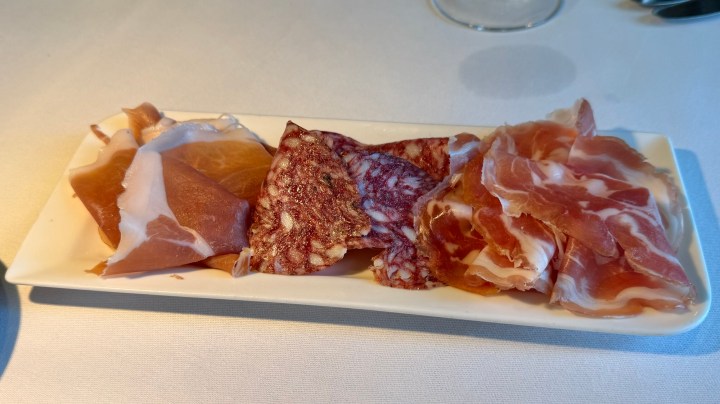 A plate of assorted cured meats, including slices of prosciutto, salami, and other deli meats, arranged neatly on a white platter.