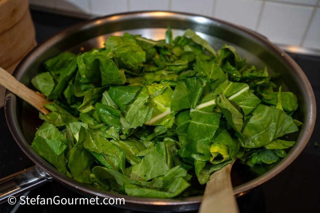 Freshly chopped greens in a stainless steel pan with a wooden spoon.