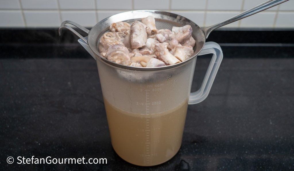 A measuring jug filled with strained broth and solid ingredients, placed on a dark countertop.