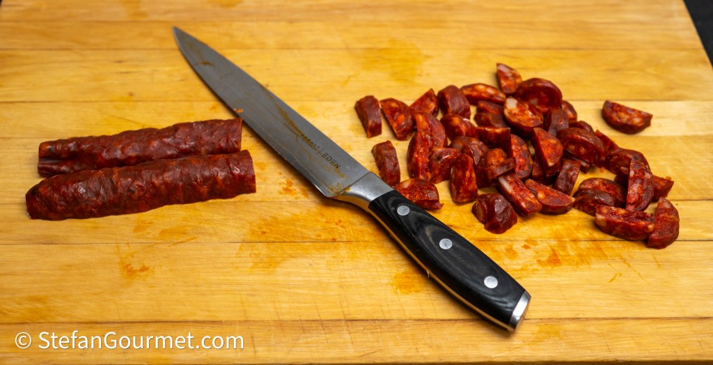 A wooden cutting board with sliced chorizo sausage and a chef's knife.