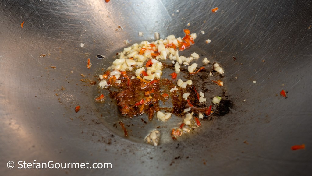Sautéed garlic and red chili pieces in a stainless steel wok.