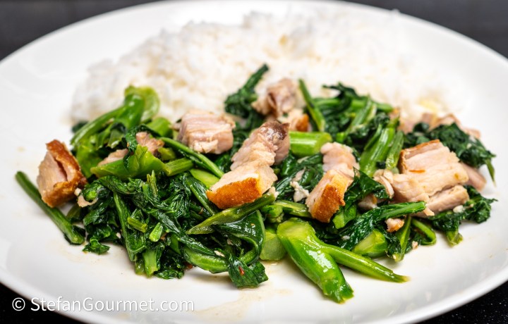 A plate of stir-fried greens with pieces of pork, served alongside fluffy white rice.