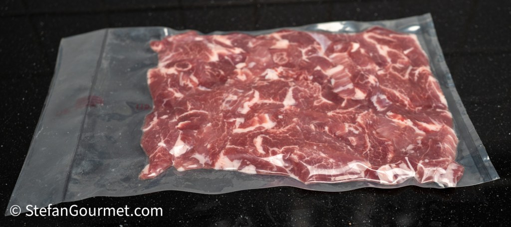 Vacuum-sealed package containing raw marbled meat on a black countertop.