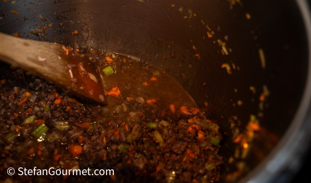 Cooked ground meat and chopped vegetables simmering in a pot with a wooden spoon stirring.