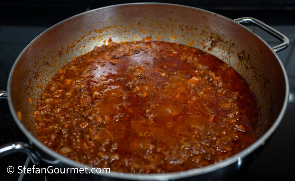 A large pot filled with a rich, simmering meat sauce on a stovetop.