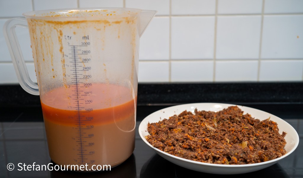A clear measuring jug filled with a layered sauce, next to a plate of finely chopped, cooked meat mixture with visible vegetable pieces.