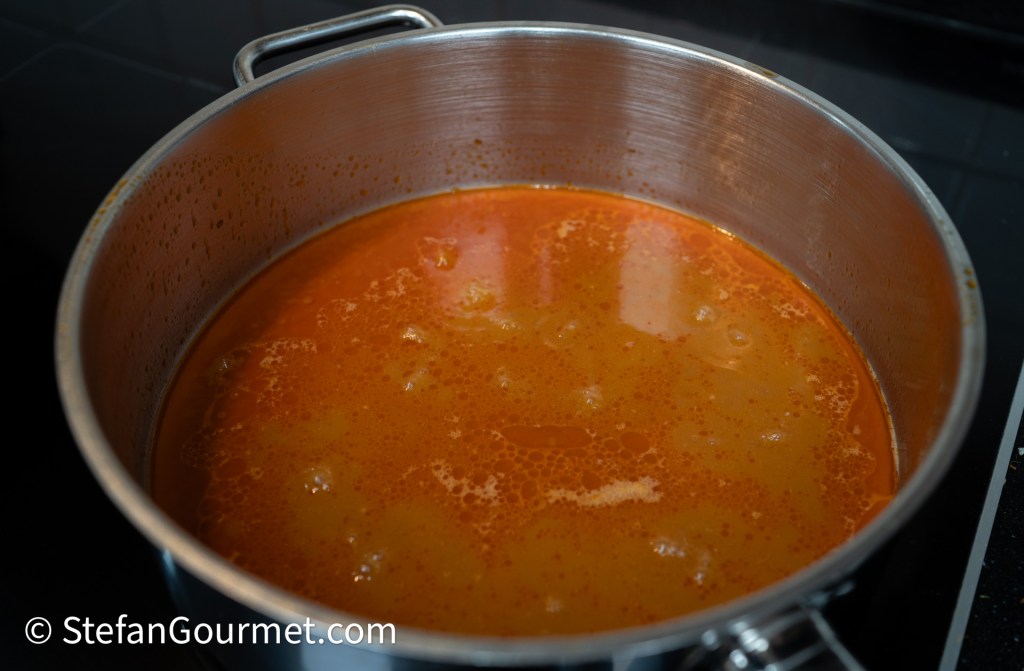 A stainless steel pot filled with bubbling orange sauce on a stove.