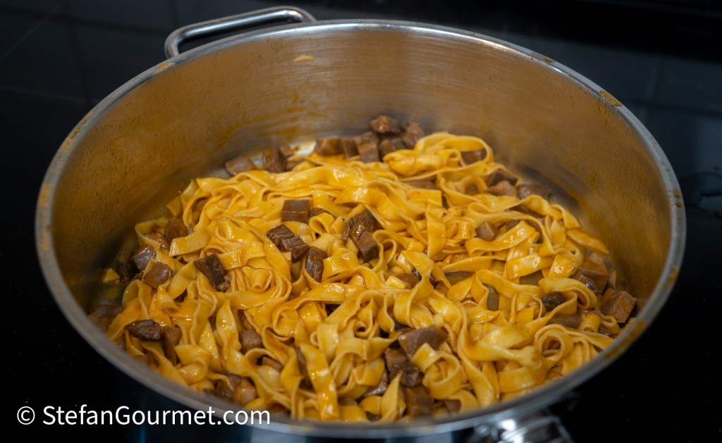 A pot filled with cooked fettuccine pasta mixed with chunks of beef, coated in a savory sauce.