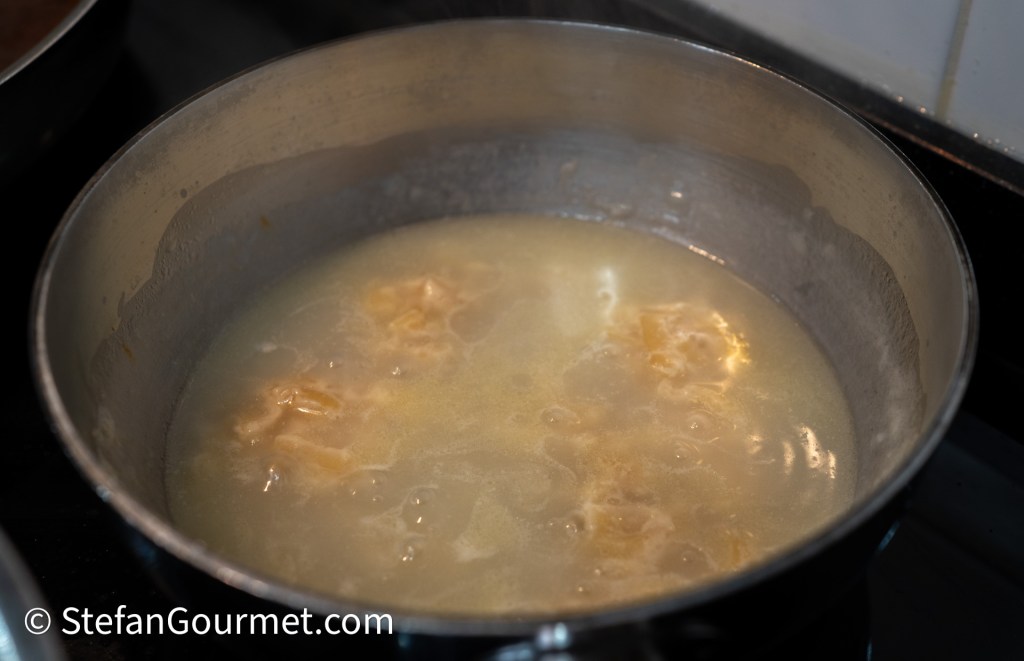 A close-up of a pot filled with boiling water and dumplings on a stovetop.