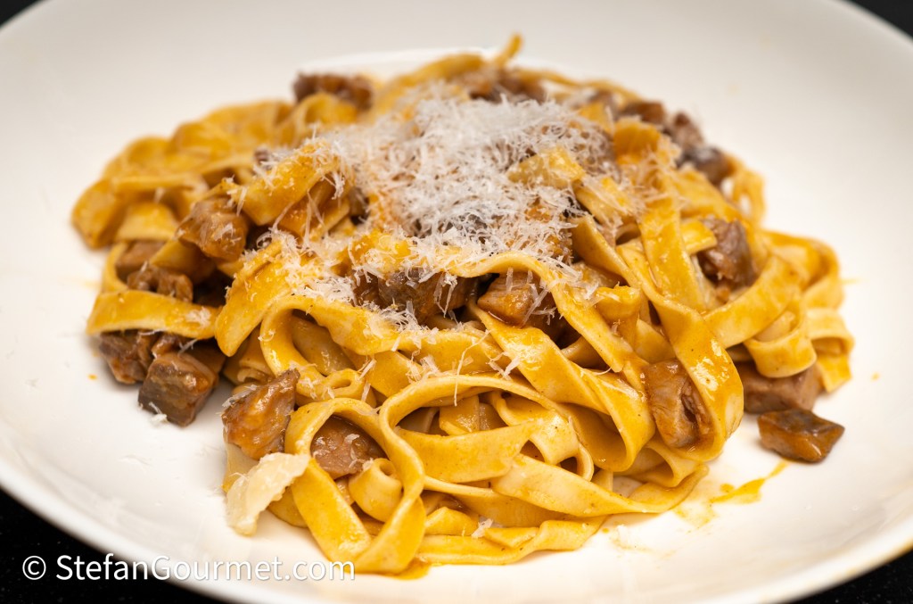 A plate of fettuccine pasta topped with shredded cheese and cooked mushrooms.