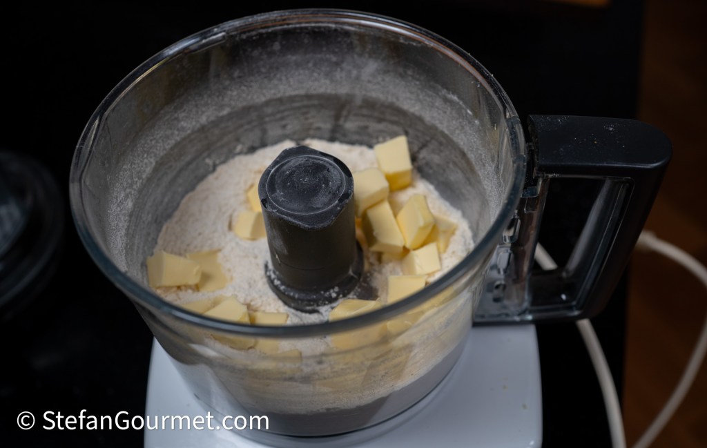 A food processor containing flour and chunks of butter, ready for mixing.