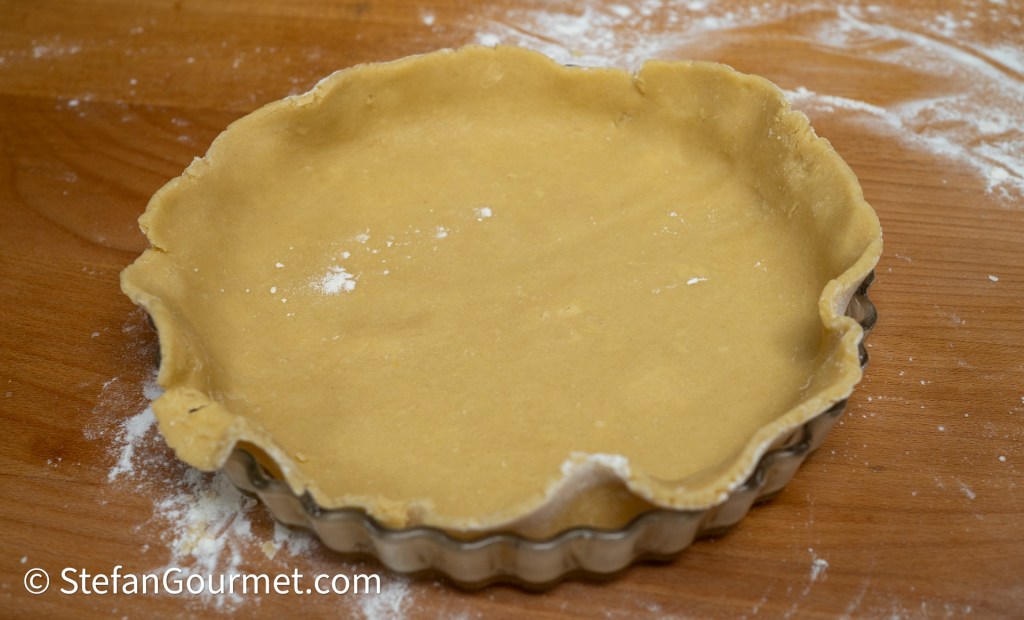 Unbaked pie crust in a tart pan on a wooden surface, lightly dusted with flour.