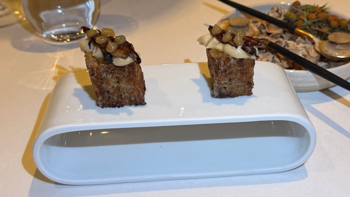 Two small pieces of savory bread topped with creamy spread and garnished with chopped ingredients, served on a sleek white platter.