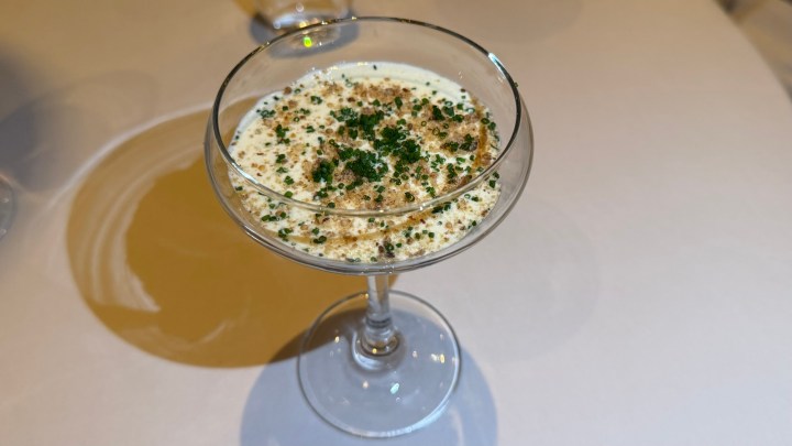 A small cocktail glass filled with a creamy dessert topped with crushed brown sugar and herbs.