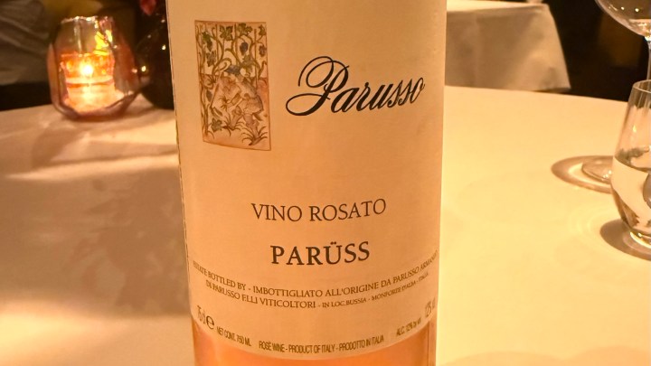 Close-up of a bottle of Parusso Vino Rosato wine with a decorative label, placed on a table with a soft-lit background.